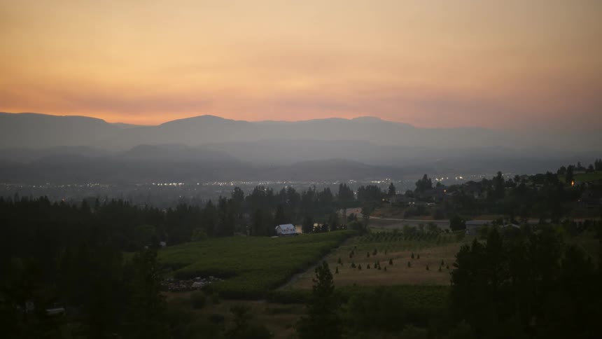 Vehicle moves along road toward town passing forest and fields under red sky on a foggy day