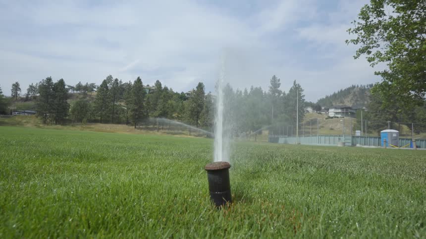Sprinkler sprays water onto green grass in football field and pops back into the ground