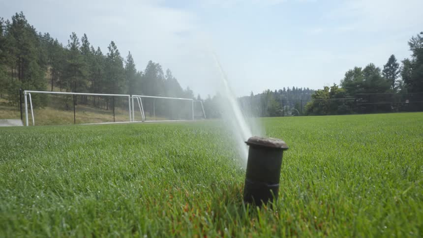 Sprinkler sprays water onto green grass in football field