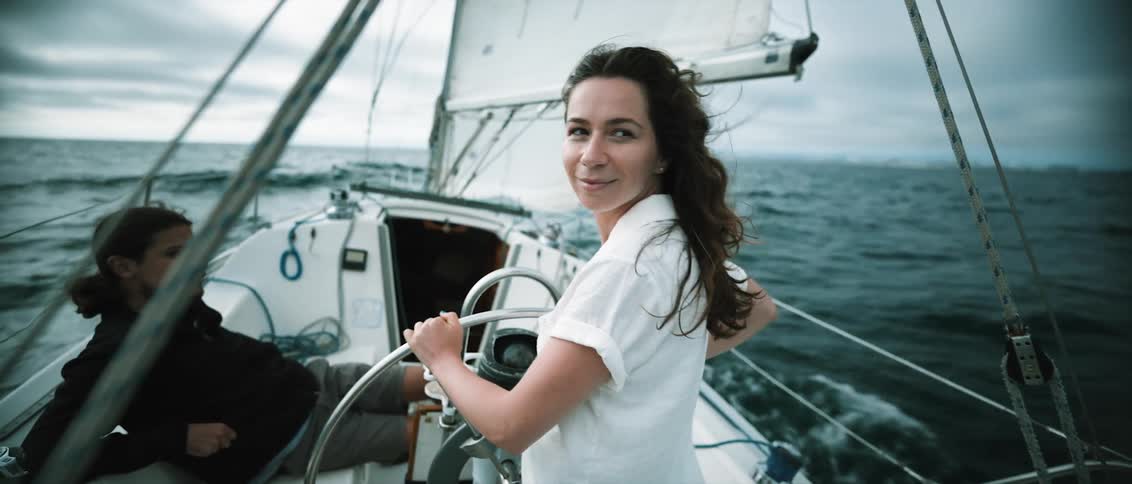 A woman sailing in the ocean looks back behind her as the boat crashes through waves