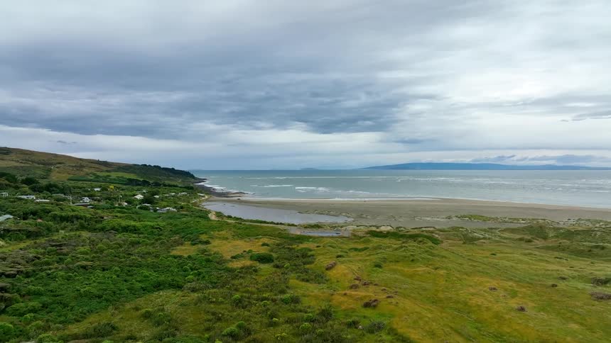 Neighborhood houses sit along the coast as waves roll in over the beach under a cloudy sky