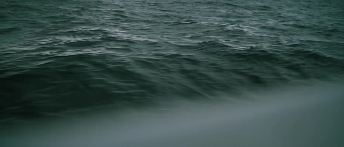 Sailboat moving through ocean swell with clouds in the distance