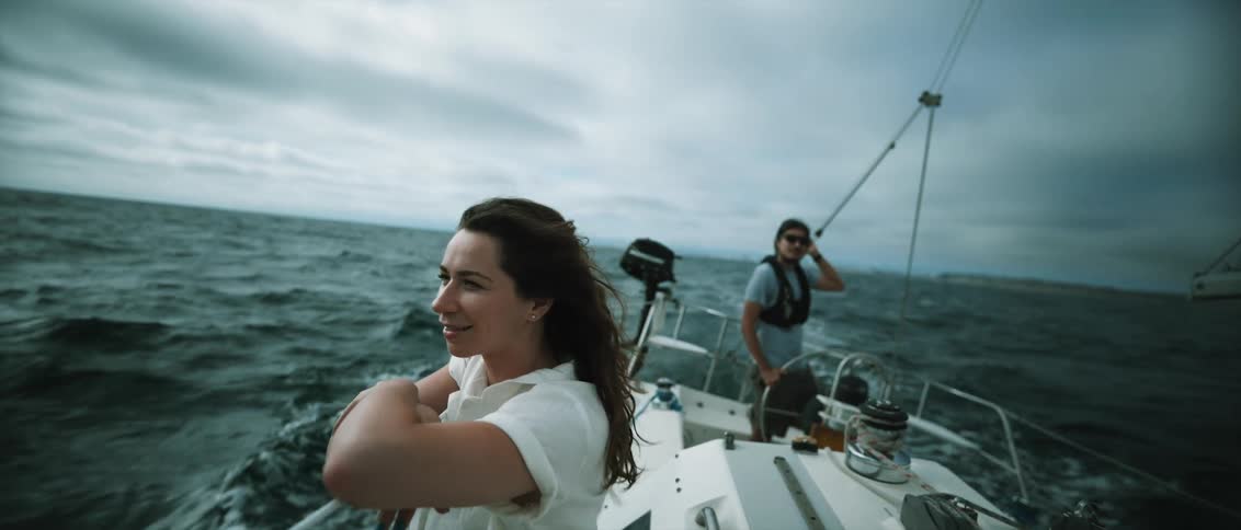 A woman looks off the side of a sailboat in the ocean