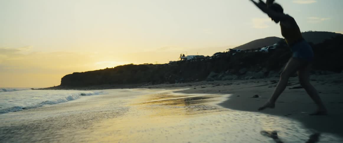 Female does gymnastics across the beach as the camera pushes in