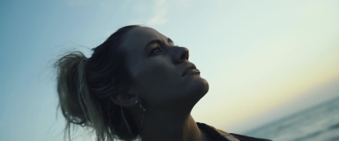 Woman with tattoo looks up at the sunset over the ocean