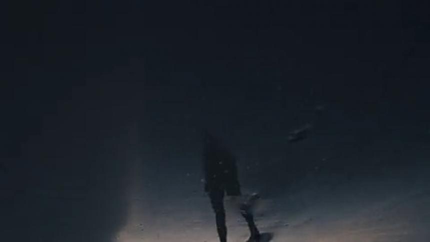 A woman's reflection walks across wet sand