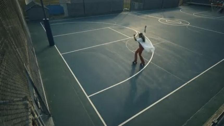 A long white shirt billows behind a woman roller skating on an empty basketball court