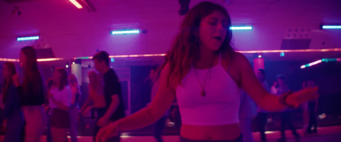 A teenage girl dances on roller skates as other skate around her at a roller rink
