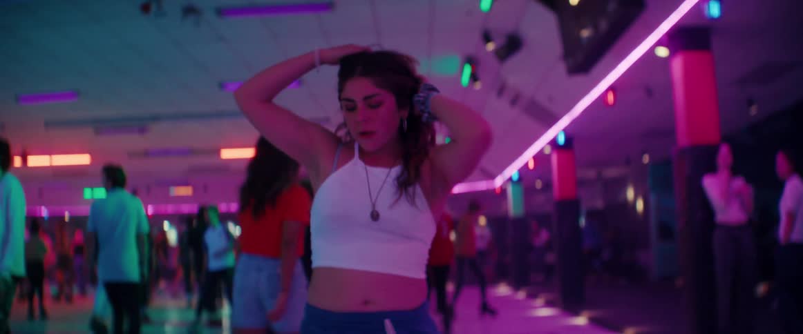 A young woman skates backwards with ease at a crowded indoor roller rink