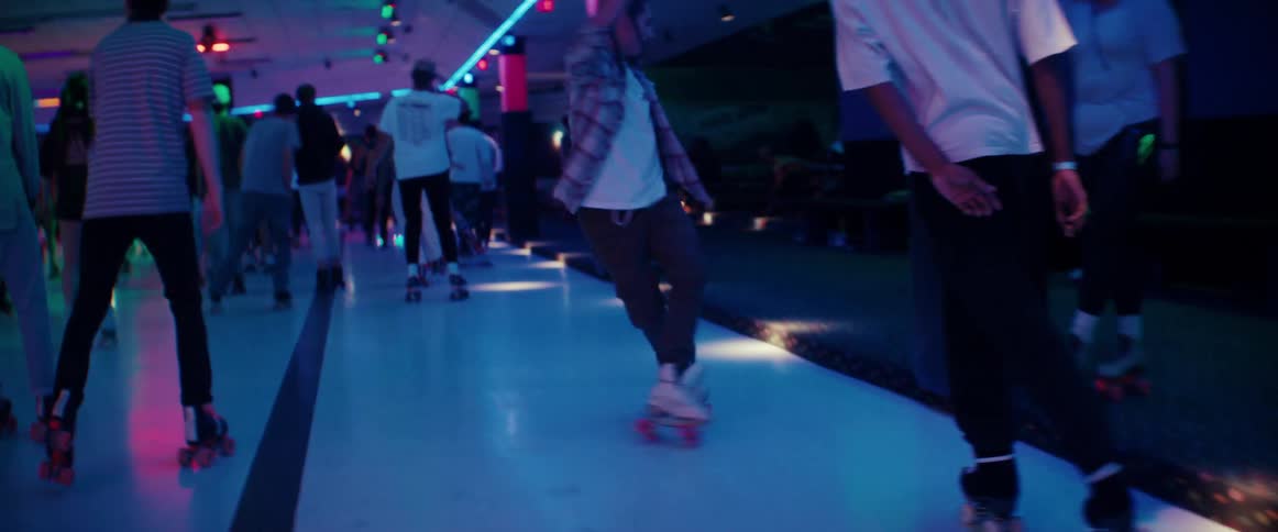 Young man dancing in roller skates on a rink filled with people under colorful lights