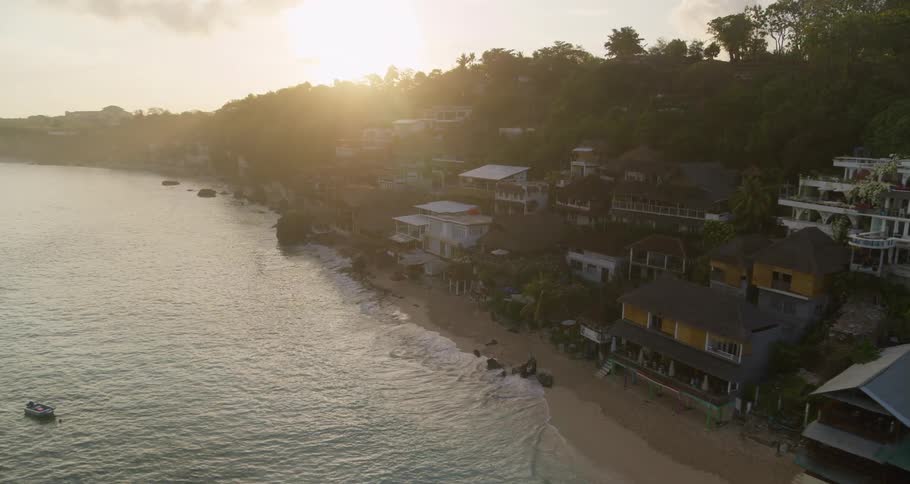 Ocean waves splash against the sandy shore with homes and apartments built into the tree covered slope