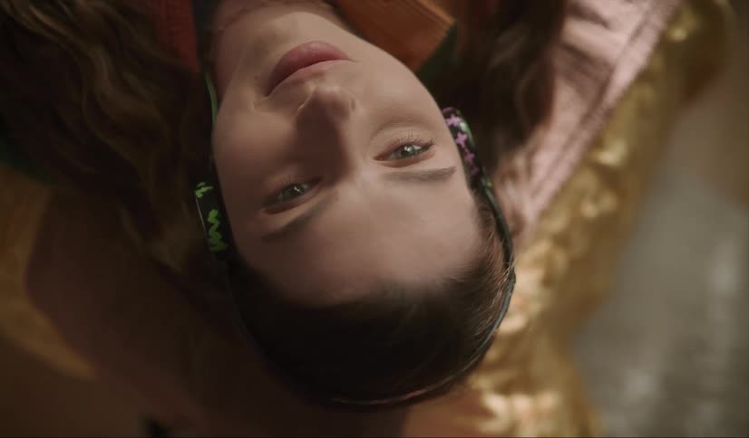 A woman is laying on a bed listening to headphones