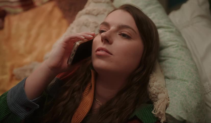 A woman is lying down on pillows as she talks on her phone