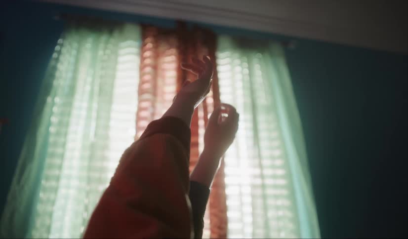 Woman with colorful sweater lies on bed holding up arms next to window