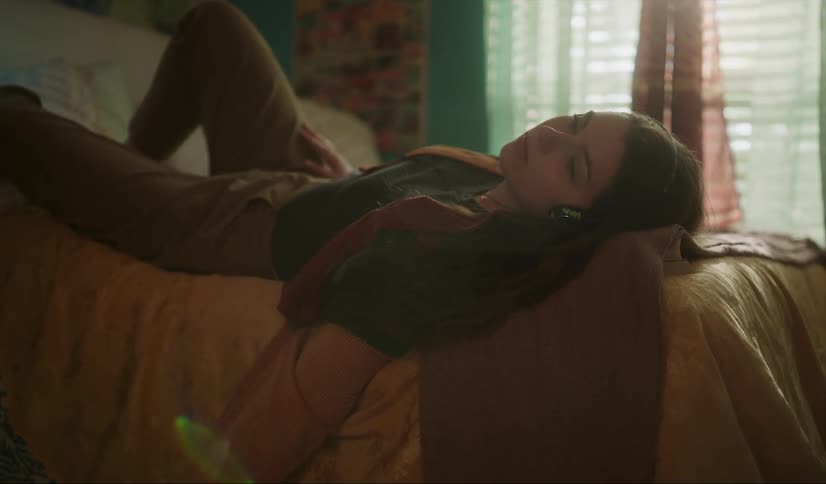 A woman lying in bed listening to music on her headphones tapping her fingers on her leg