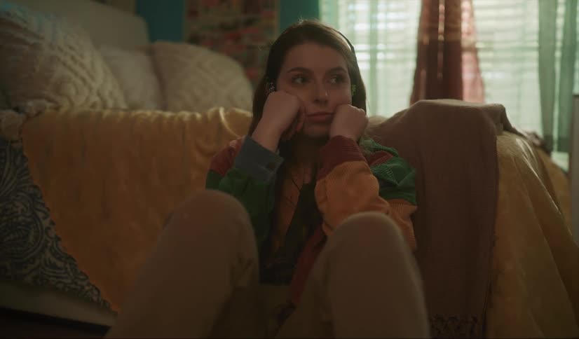 A sad looking teenage girl leans against a couch at home and rests her face in her hands