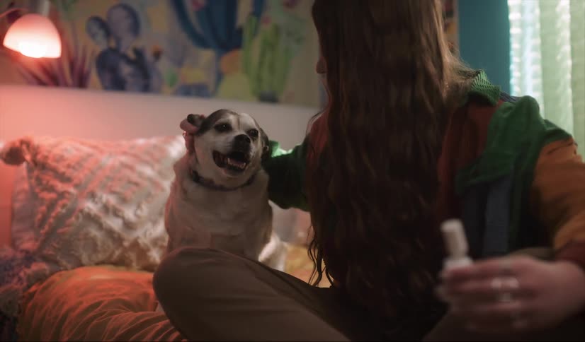 A woman pets her dogs head while sitting in bed