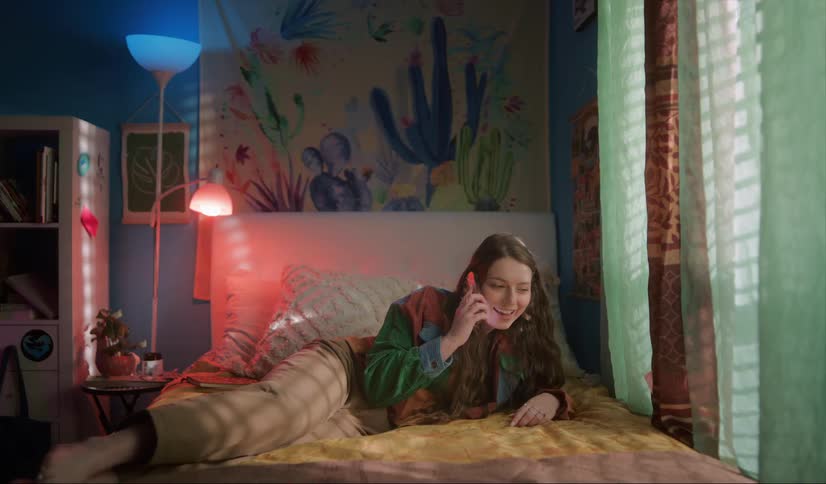 Young happy woman takes a call in her smartphone while laying in bed at home
