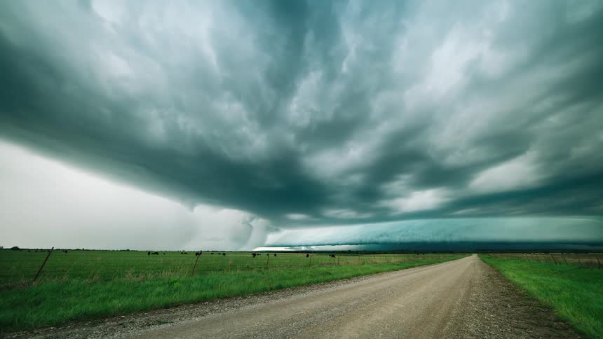 Storm clouds roll in over a rural road as a scud cloud moves in from the distance