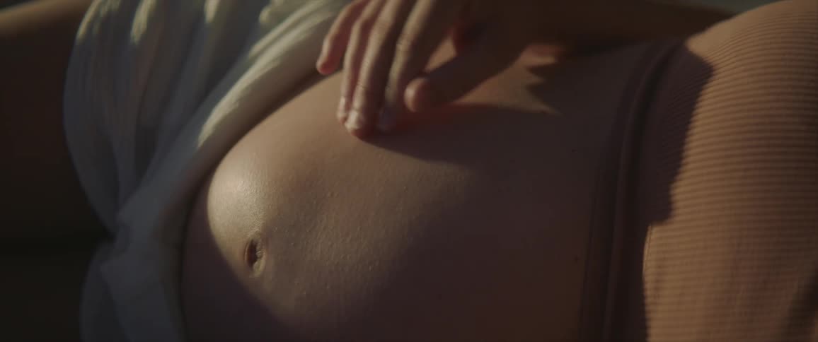Close up of a pregnant woman sitting at home rubbing her belly with a hand while the baby moves