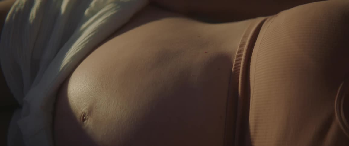 Blonde pregnant mother with brown top and white shorts lies on bed and baby kicking in womb