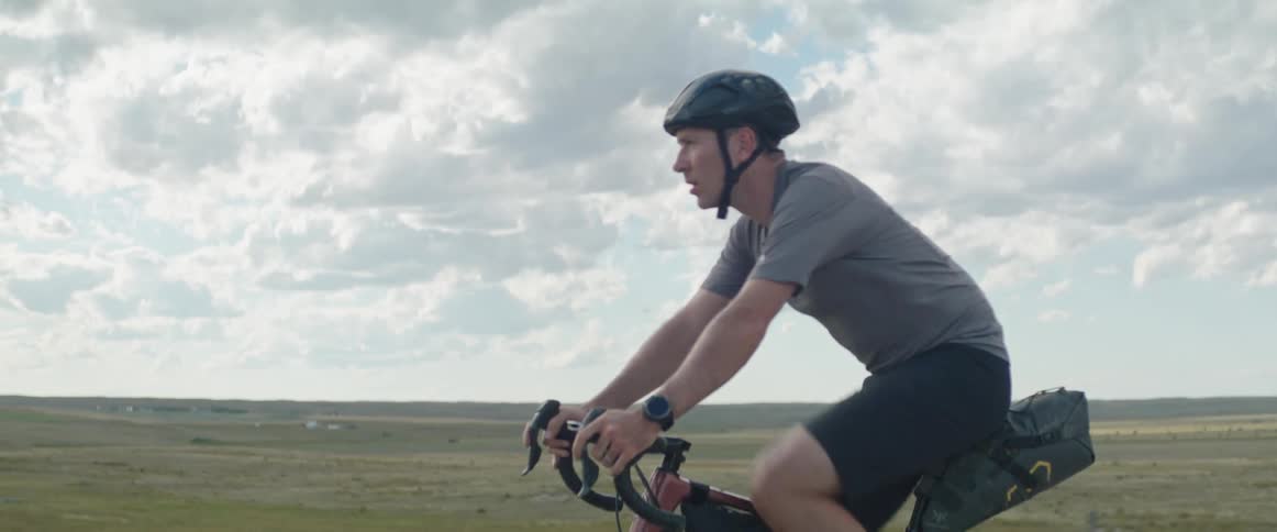 Mature man wearing a helmet rides a bicycle on a rural road at daytime under a blue sky