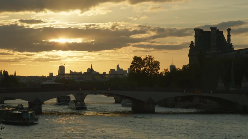 Vehicles driving across a bridge and boats in the river below with a skyline in the distance