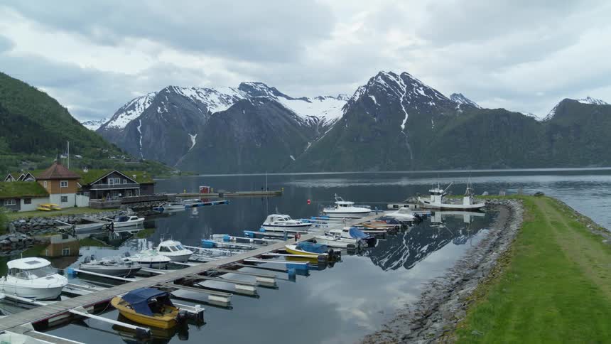 Boats docked in Norwegian fjord with snow capped mountains