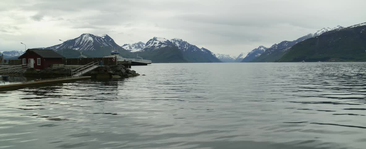 View of cal lake and distant boat sailing on water next to snowy mountains on cloudy day