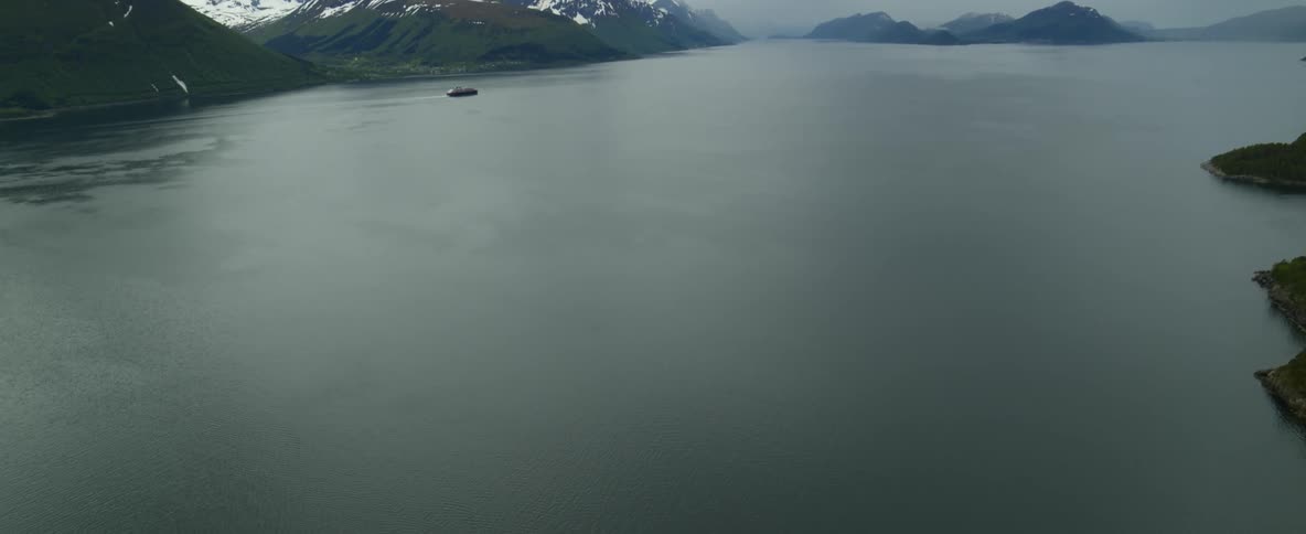 A ferry ship in the fjord water with snow dusted mountain ridges and peaks