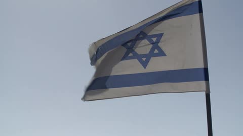 A white and blue flag blows in the wind of a clear sky