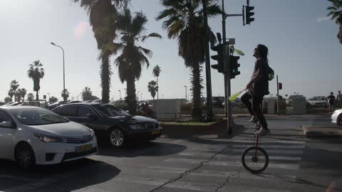 A man is in the street on a unicycle juggling