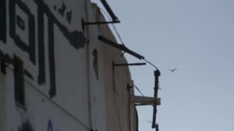 A plane flies over a wall covered in graffiti