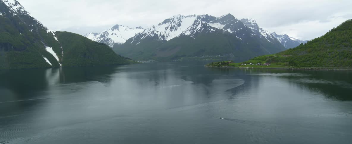 A boat makes its way across the fjord with mountain and green hills