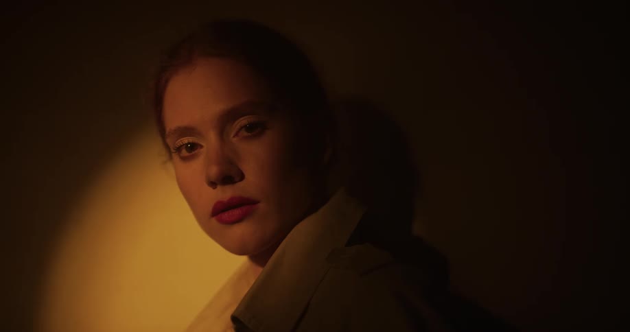 Woman with ponytail and brown coat stands in spotlight