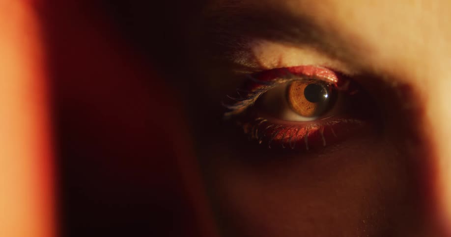 Orange light shines on a womans face as she opens her brown eye and looks around