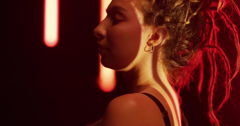 Young woman with a chaotic hairdo stands on a room surrounded by floating lights looking at the camera
