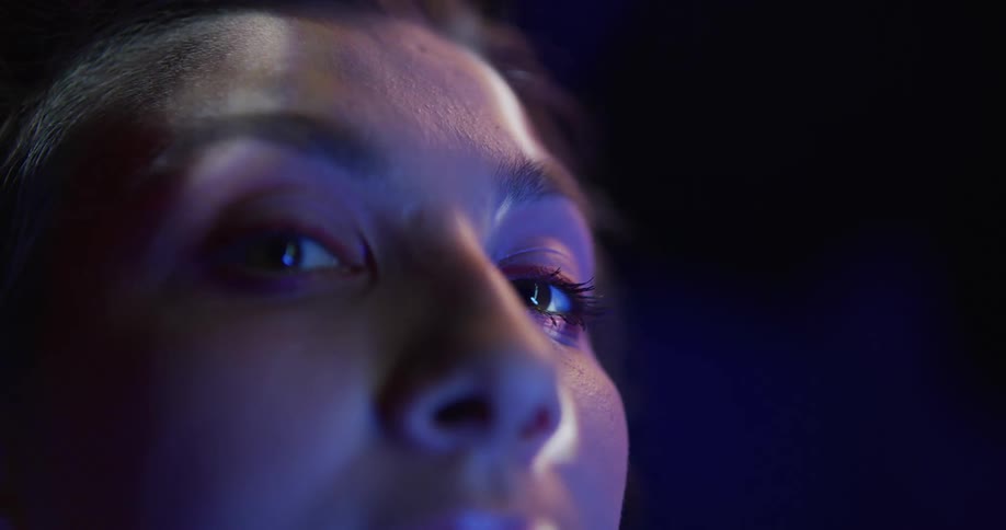 Close up of the face of a woman slowly turning to look at the camera under red and blue lights