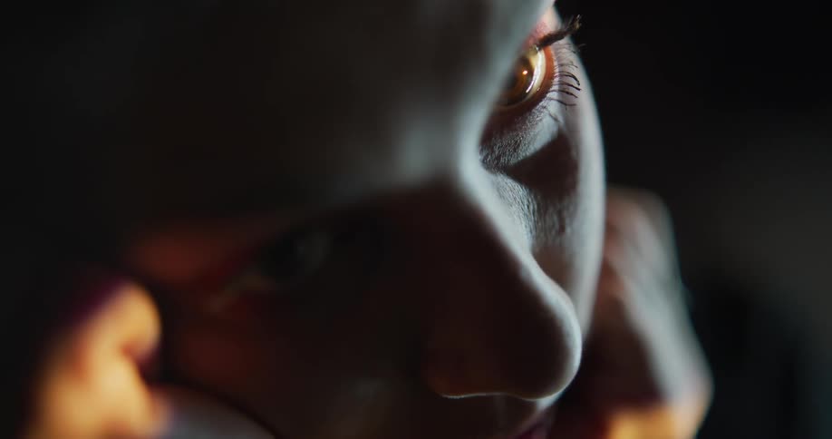 Close up of light reflecting on the eyes of a woman looking at the camera inside a dark room