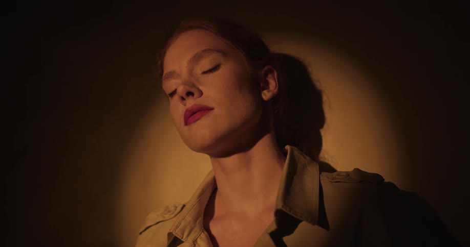 A woman leans her head back on against a wall with her eyes closed and then opens her eyes and smiles