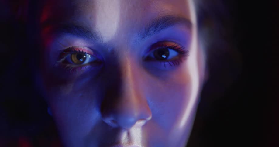 Face of a young woman illuminated by a white and red light in a dark room