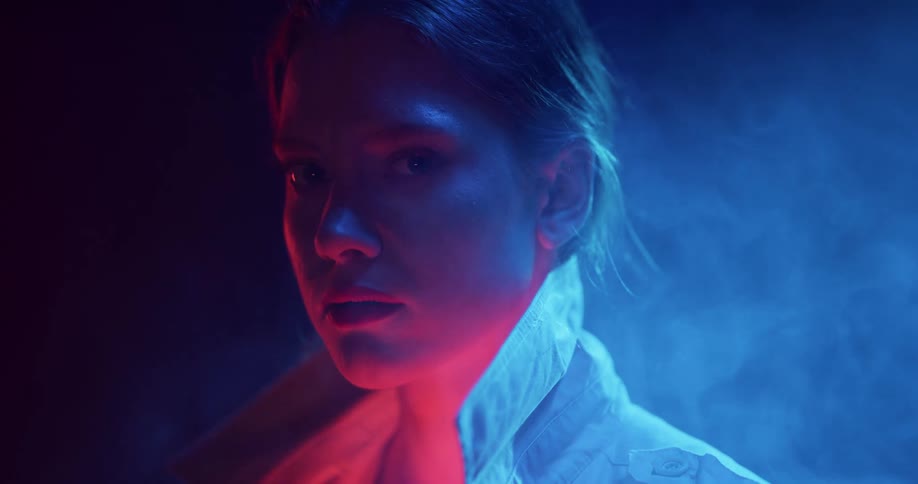 A woman is standing outside in the darkness as light illuminates the smoke rising behind her