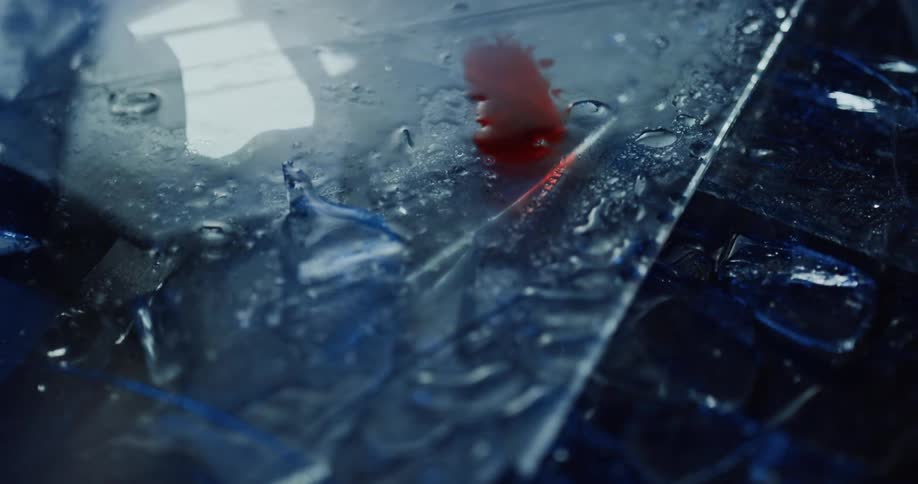 An emergency red light flashes on shards of broken glass and metal spotted with blood