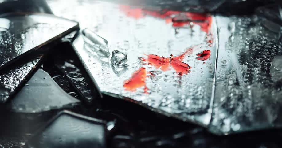 Close up of broken glass pieces with blood and police lights displaying on at the crime scene