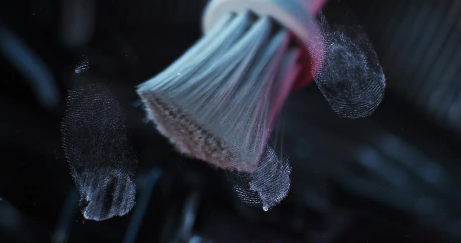 A brush is moving over a window leaving powder on fingerprints so they are visible