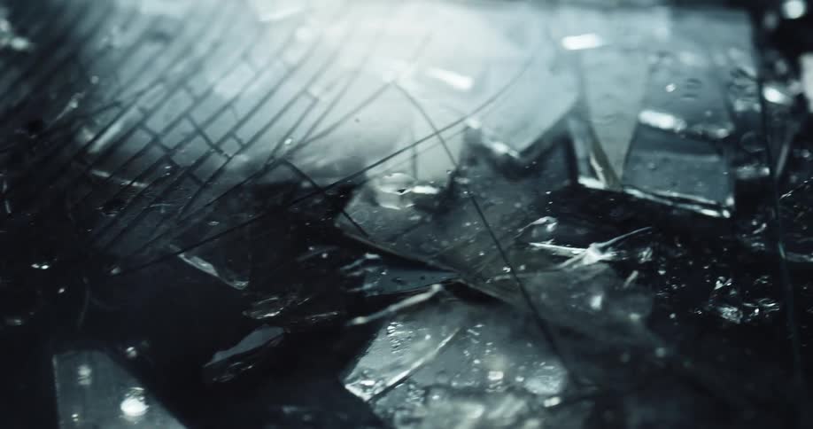 Shattered and cracked glass with shards of metal dotted with rain drops