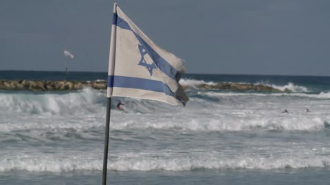 An israeli flag billows on a beach