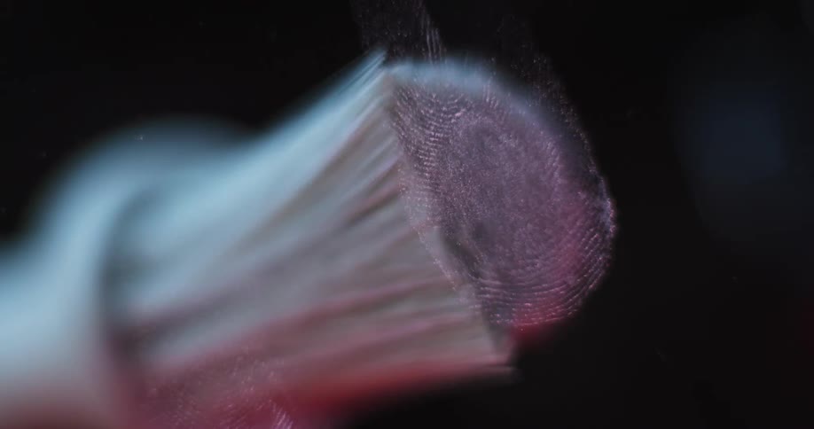 A person uses a brush to reveal fingerprints on the surface of a window pane