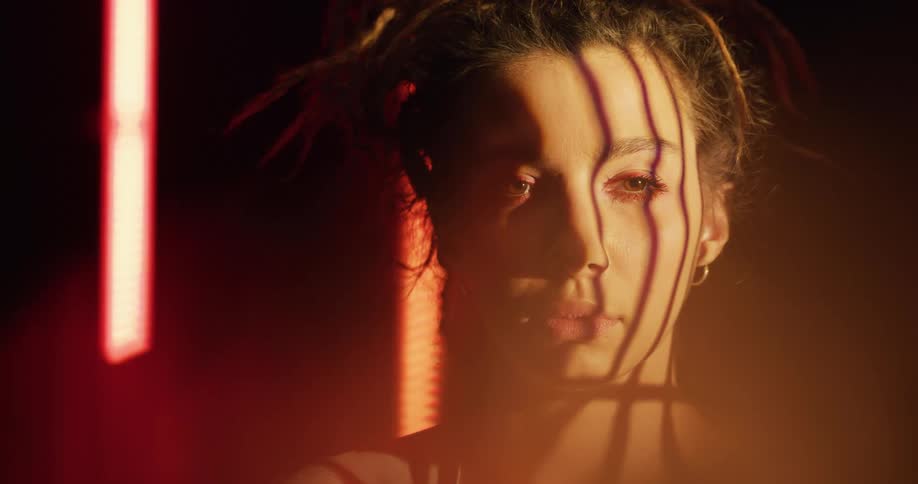 Close up of shadows on the face of a young woman standing inside a dimly lit room looking at the camera