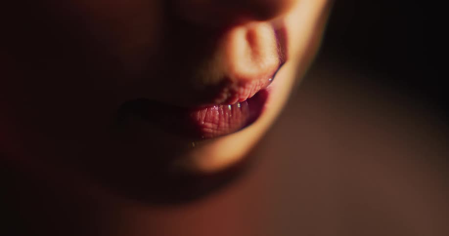 Close up of the red plump lips of a woman inside a dimly lit room